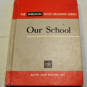 May include: A vintage book titled "Our School" from The Sheldon Basic Reading Series. The book cover is gray with red accents and features the publisher's logo, Allyn and Bacon, Inc.