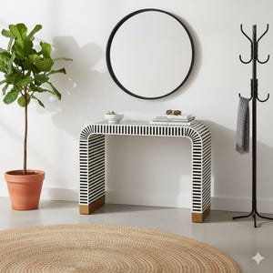 Puede incluir: Una escena de entrada moderna con una consola a rayas blancas y negras, detalles dorados y un espejo redondo con marco negro. Una planta en maceta, un perchero y una alfombra tejida completan la decoración. La mesa mide unos 120 cm de largo.