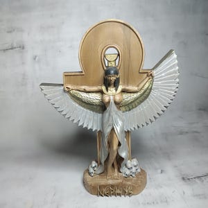 Peut inclure: Statue détaillée de la déesse égyptienne Nephthys, avec des ailes argentées déployées et une robe argentée fluide. La statue a un fond couleur bois avec le symbole hiéroglyphique. La base porte le nom "Nephthys" gravé.
