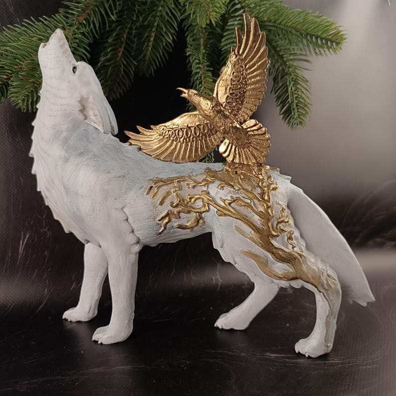 May include: A white wolf figurine with a howling pose, adorned with gold-colored accents. A gold eagle sculpture is perched on the wolf's back, with a tree-like design. The sculpture is set against a dark background with evergreen branches.