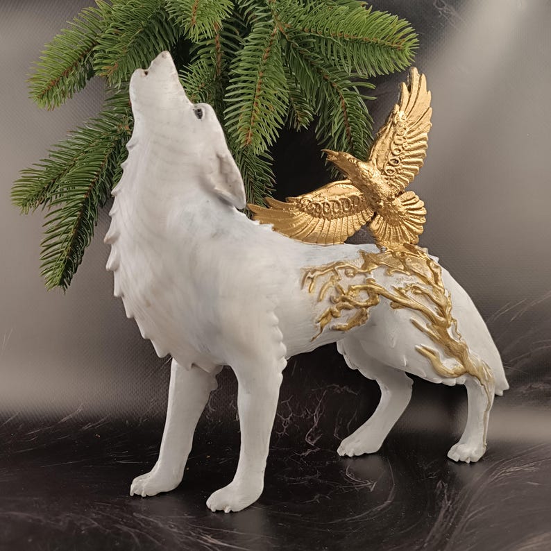 May include: A white wolf figurine with a howling pose, adorned with a gold eagle and gold branch accents. The sculpture is set against a dark background with a sprig of green foliage, creating a striking contrast.