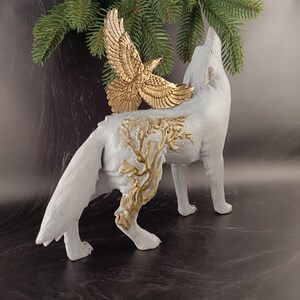 May include: A white wolf figurine with a gold eagle attached to its back. The wolf is in a howling pose, with gold tree-like designs on its side. The eagle has outstretched wings. The figurine is a decorative item.