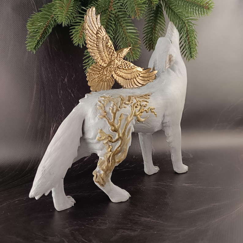 May include: A white wolf figurine with a gold eagle attached to its back. The wolf is in a howling pose, with gold tree-like designs on its side. The eagle has outstretched wings. The figurine is a decorative item.