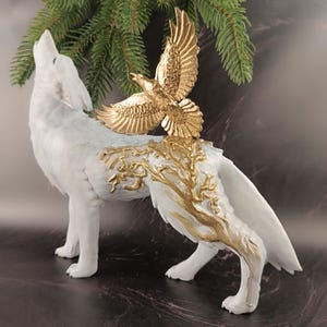 May include: A white wolf figurine with a gold eagle perched on its back. The wolf is howling, and the sculpture features gold tree-like accents on its body. The eagle has outstretched wings, and the sculpture is set against a dark background.