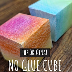 May include: A colorful, ombre-style paper cube with the text "The Original No Glue Cube" on the front. The cube is made of paper and is a craft project.
