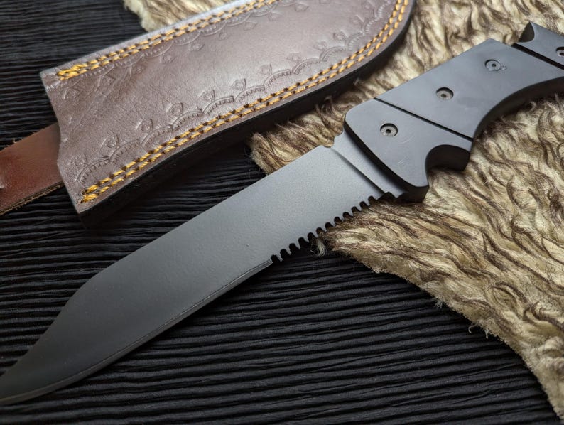 May include: A black knife with a serrated edge and a dark handle. The knife is partially sheathed in a brown leather case with decorative stitching. The blade is angled towards the viewer.