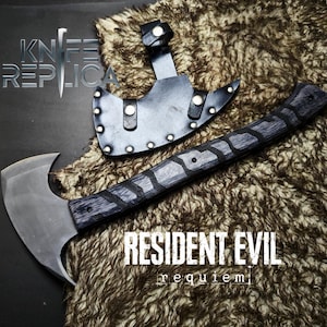 May include: Axe replica with a black and gray handle and a silver blade, accompanied by a black leather sheath. The text "RESIDENT EVIL requiem" is visible. The axe is displayed on a textured, brown surface.