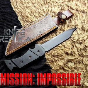 May include: A tactical knife with a silver blade and a black handle, resting on a textured surface. The knife is accompanied by a brown leather sheath with decorative stitching. The text "MISSION: IMPOSSIBLE" is displayed in red.