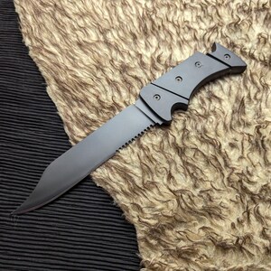 May include: A gray knife with a serrated edge and a curved handle. The blade is angled and the handle has a series of small, circular rivets. The knife is resting on a textured, tan surface.