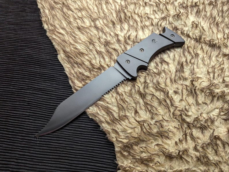 May include: A gray knife with a serrated edge and a curved handle. The blade is angled and the handle has a series of small, circular rivets. The knife is resting on a textured, tan surface.