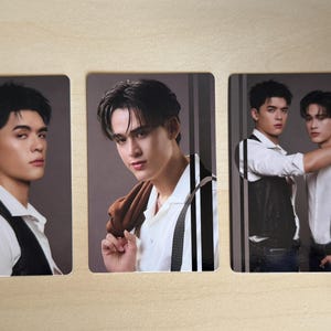 Puede incluir: Tres tarjetas rectangulares con retratos de hombres j&oacute;venes. Los hombres visten camisas blancas, chalecos y tirantes. Un hombre sostiene una chaqueta marr&oacute;n sobre su hombro. Las tarjetas est&aacute;n dispuestas sobre una superficie de madera clara.