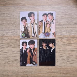 May include: Four rectangular trading cards featuring portraits of young men in various outfits. The top left card shows two men in tan jackets. The top right card shows two men in tan jackets with a purple emblem. The bottom left shows two men in dark jackets. The bottom right shows two men in black.