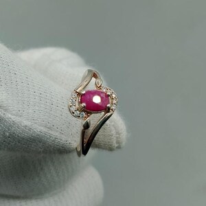Peut inclure: Bague en or rose ornée d'un grand rubis ovale, entouré de petites pierres d'accent claires. La bague présente un design ajouré délicat avec une monture fendue.
