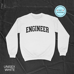 Puede incluir: Sudadera unisex blanca con la palabra "ENGINEER" en letras negras y en negrita en el pecho. La sudadera de manga larga tiene cuello redondo. Las palabras "UNISEX WHITE" están impresas en la parte inferior. Una insignia de "FAST SHIPPING" está en la esquina superior derecha.
