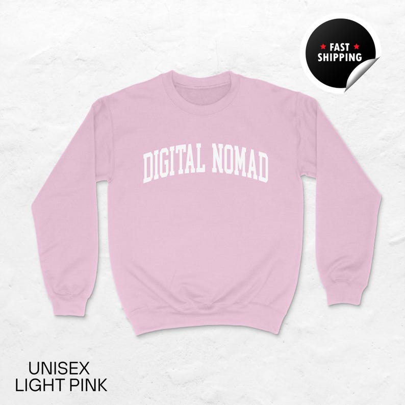 May include: A light pink unisex sweatshirt with the text "DIGITAL NOMAD" in white block letters across the chest. The sweatshirt has long sleeves and a crew neck. The words "UNISEX LIGHT PINK" are printed at the bottom.