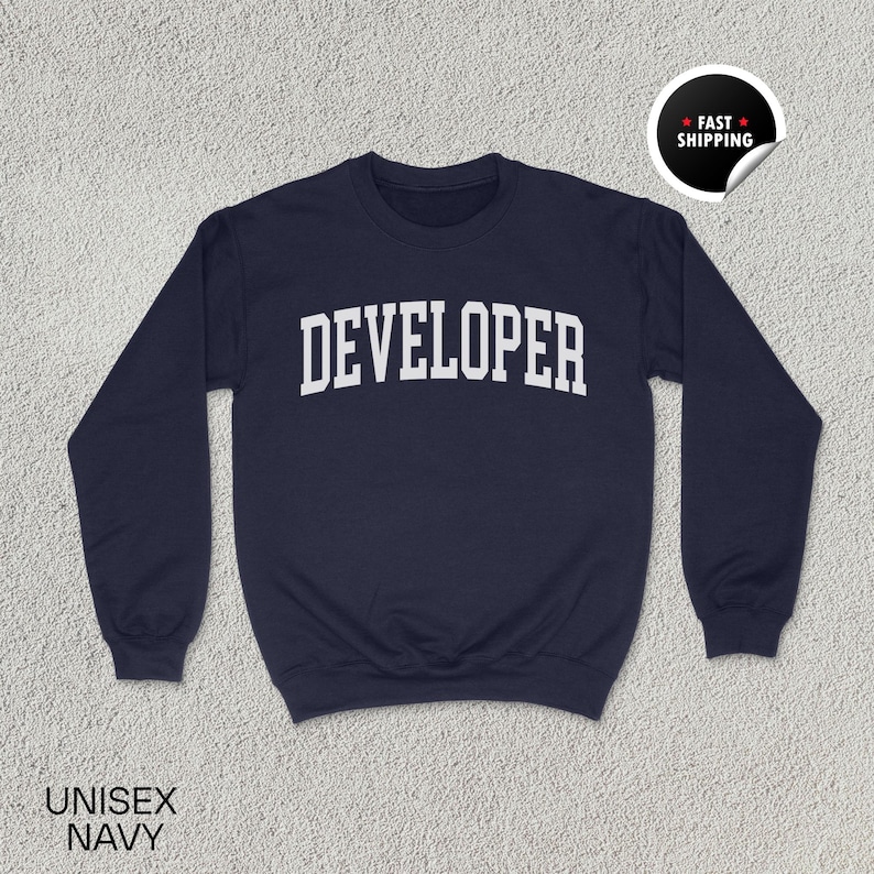 May include: Navy blue unisex sweatshirt with the word "DEVELOPER" in white, arched lettering. The sweatshirt has a crew neck and long sleeves. The words "UNISEX NAVY" are printed at the bottom left. A "FAST SHIPPING" sticker is on the top right.