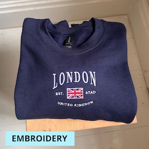May include: Navy blue sweatshirt with white embroidered text that reads "LONDON EST. 47AD UNITED KINGDOM" and a red, white, and blue embroidered flag.