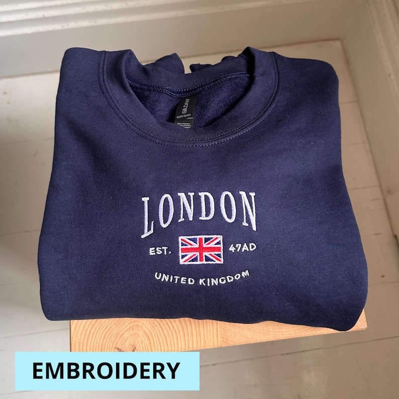 May include: Navy blue sweatshirt with white embroidered text that reads "LONDON EST. 47AD UNITED KINGDOM" and a red, white, and blue embroidered flag.
