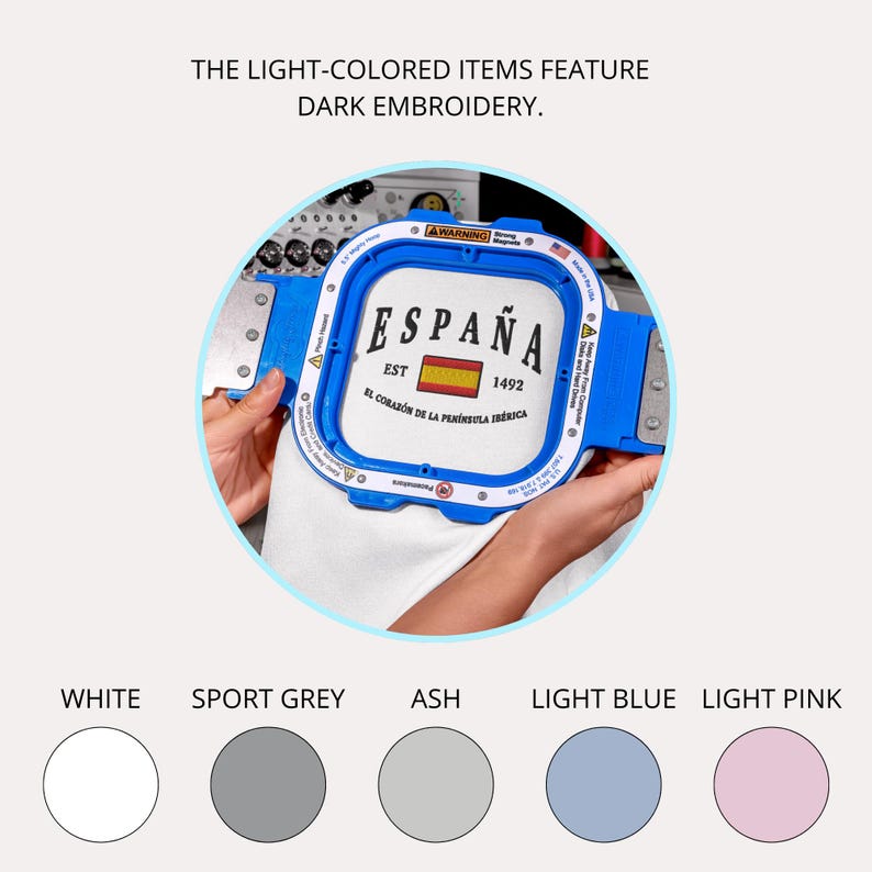 May include: A white fabric is held in a blue embroidery hoop. The fabric features the word "ESPA&Ntilde;A" with a Spanish flag and the text "EST 1492". The text "EL CORAZ&Oacute;N DE LA PEN&Iacute;NSULA IB&Eacute;RICA" is also visible. Color swatches of white, sport grey, ash, light blue, and light pink are shown.