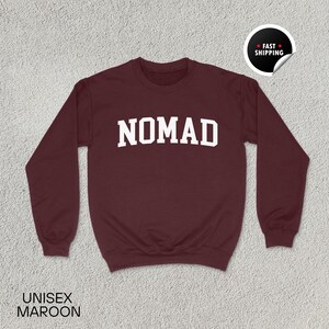 May include: Maroon unisex sweatshirt with the word "NOMAD" in bold white letters across the chest. The sweatshirt has a crew neck and long sleeves. A "Fast Shipping" sticker is in the upper right corner. The text "UNISEX MAROON" is at the bottom.