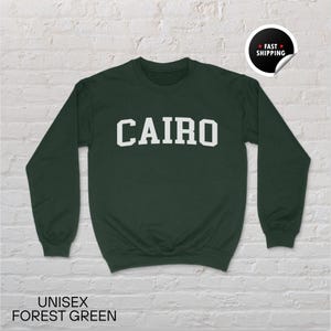 May include: Forest green unisex sweatshirt with the word "CAIRO" in white block letters. The sweatshirt has long sleeves and a crew neck. The words "UNISEX FOREST GREEN" are printed at the bottom of the image.