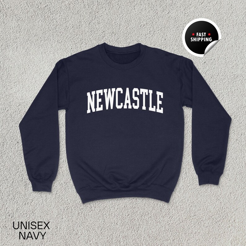 Puede incluir: Sudadera unisex azul marino con la palabra "NEWCASTLE" en letras blancas en el pecho. La sudadera tiene cuello redondo y mangas largas. Una pegatina de "Env&iacute;o r&aacute;pido" est&aacute; en la esquina superior derecha. Las palabras "UNISEX NAVY" est&aacute;n en la parte inferior.
