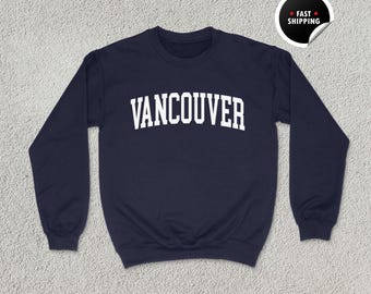 May include: Navy blue unisex sweatshirt with the word "VANCOUVER" in white, arched lettering. The sweatshirt has a crew neck and long sleeves. A "Fast Shipping" sticker is in the upper right corner. The words "UNISEX NAVY" are at the bottom.