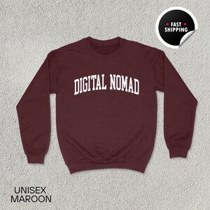 May include: Maroon unisex sweatshirt with the text "DIGITAL NOMAD" in white, arched across the chest. The sweatshirt has long sleeves and a crew neck. A "Fast Shipping" sticker is in the upper right corner. The word "UNISEX" and the color "MAROON" are printed at the bottom.