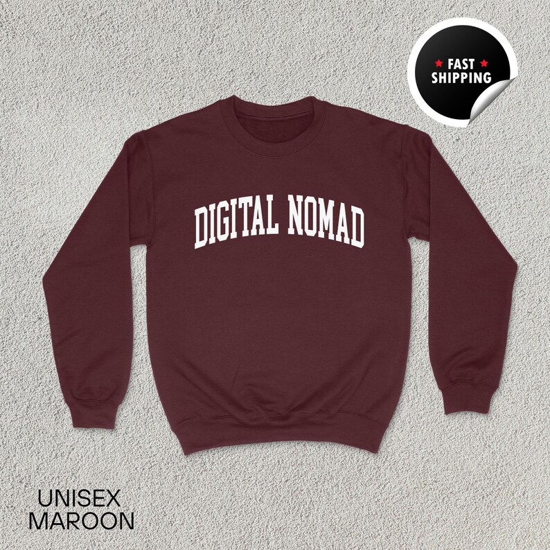 May include: Maroon unisex sweatshirt with the text "DIGITAL NOMAD" in white, arched across the chest. The sweatshirt has long sleeves and a crew neck. A "Fast Shipping" sticker is in the upper right corner. The word "UNISEX" and the color "MAROON" are printed at the bottom.
