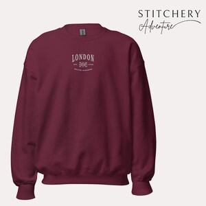 May include: A maroon sweatshirt with a white embroidered design that says "LONDON EST 1948 UNITED KINGDOM" with a small embroidered Union Jack flag.