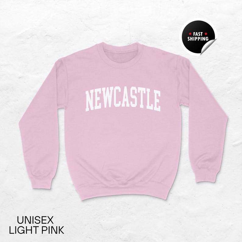 Puede incluir: Sudadera unisex rosa claro con la palabra "NEWCASTLE" en letras blancas en el pecho. La sudadera tiene mangas largas y cuello redondo. El texto "UNISEX LIGHT PINK" est&aacute; en la parte inferior de la imagen. Una pegatina de "FAST SHIPPING" est&aacute; en la esquina superior derecha.