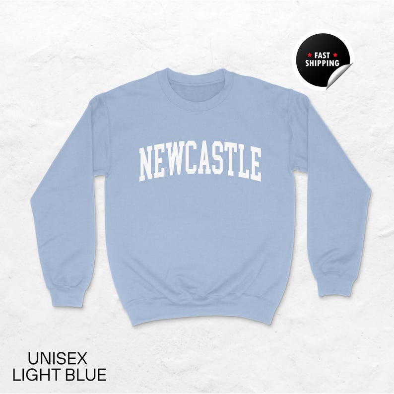 Puede incluir: Sudadera unisex azul claro con la palabra "NEWCASTLE" en letras blancas. La sudadera tiene mangas largas y cuello redondo. El texto "UNISEX LIGHT BLUE" est&aacute; en la parte inferior de la imagen. Una pegatina que dice "FAST SHIPPING" est&aacute; en la esquina superior derecha.