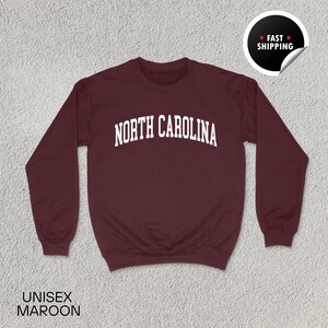May include: Maroon unisex sweatshirt with the text "NORTH CAROLINA" in white block letters. The sweatshirt has a crew neck and long sleeves. A sticker in the upper right corner says "FAST SHIPPING". The words "UNISEX MAROON" are at the bottom.