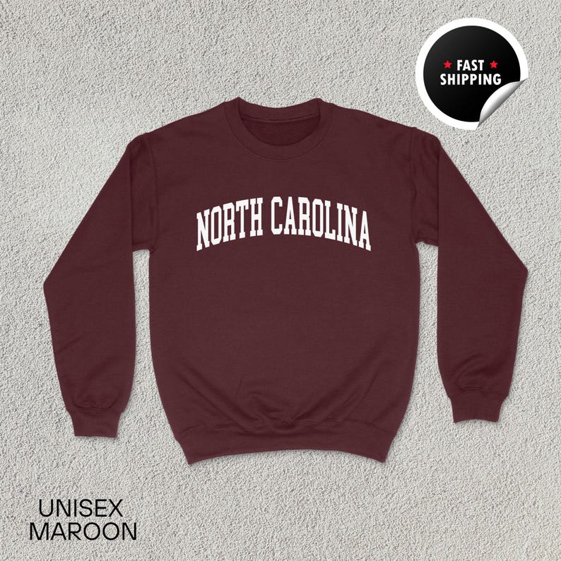 May include: Maroon unisex sweatshirt with the text "NORTH CAROLINA" in white block letters. The sweatshirt has a crew neck and long sleeves. A sticker in the upper right corner says "FAST SHIPPING". The words "UNISEX MAROON" are at the bottom.