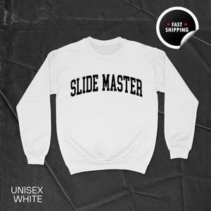 May include: A white unisex sweatshirt with the text "SLIDE MASTER" in bold, black letters across the chest. The sweatshirt has long sleeves and a crew neck. The words "UNISEX WHITE" are printed at the bottom. A "FAST SHIPPING" sticker is in the top right corner.