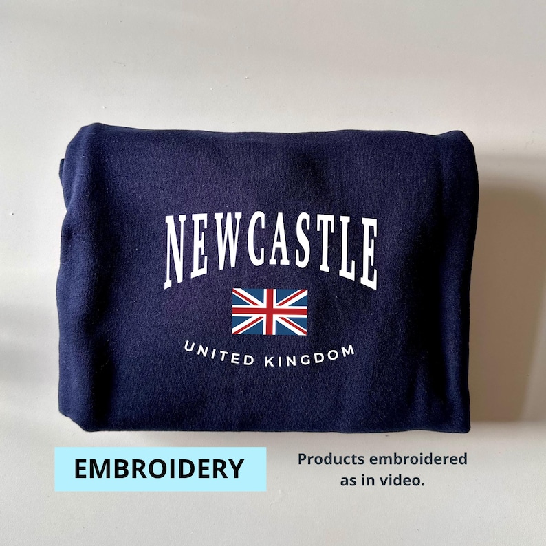 May include: A navy blue sweatshirt with white embroidery that reads "NEWCASTLE UNITED KINGDOM" and features a small embroidered Union Jack flag.