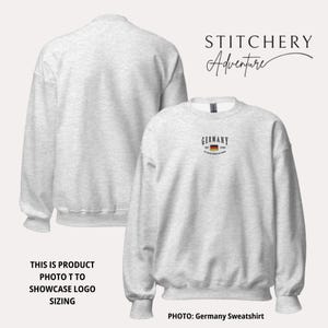 May include: Light gray sweatshirt with the word "GERMANY" and a small German flag graphic. The sweatshirt has a crew neck and long sleeves. The text "STITCHERY Adventure" is in the upper right corner. The photo showcases logo sizing.