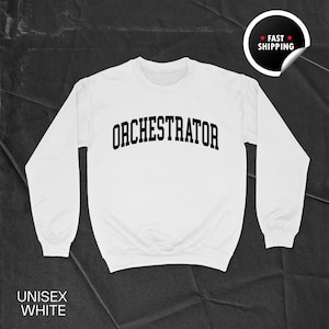 May include: A white unisex sweatshirt featuring the word "ORCHESTRATOR" in black, arched across the chest. The sweatshirt has long sleeves and a crew neck. The words "UNISEX WHITE" are printed at the bottom. A "FAST SHIPPING" sticker is in the upper right corner.