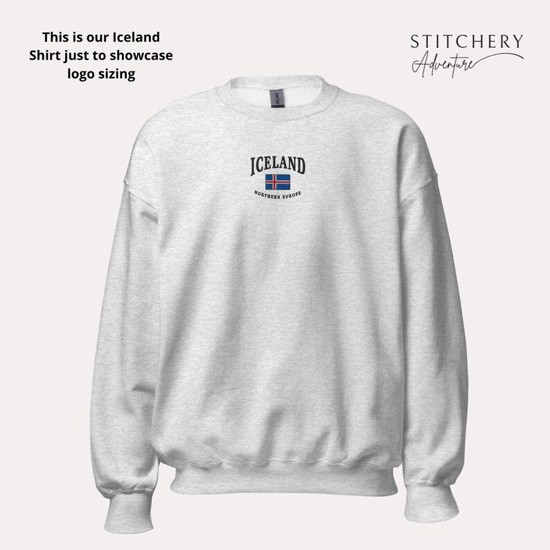 Puede incluir: Una sudadera gris claro con la palabra "ICELAND" bordada en negro sobre una peque&ntilde;a bandera islandesa. El texto "northern europe" est&aacute; debajo de la bandera. La sudadera tiene mangas largas y cuello redondo.