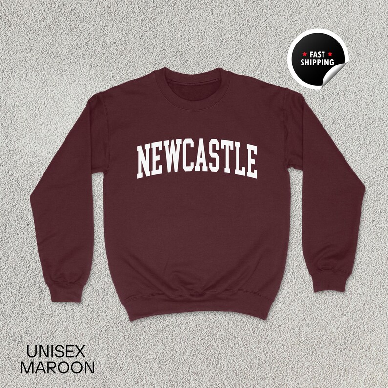 Puede incluir: Sudadera burdeos con la palabra "NEWCASTLE" en letras blancas. La sudadera tiene mangas largas y cuello redondo. Las palabras "UNISEX MAROON" est&aacute;n impresas en la parte inferior. Una pegatina de "FAST SHIPPING" est&aacute; en la esquina superior derecha.
