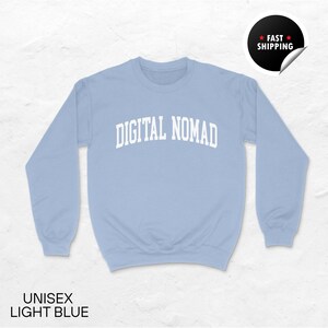 May include: Light blue unisex sweatshirt with the text "DIGITAL NOMAD" in white, arched across the chest. The sweatshirt has long sleeves and a crew neck. The words "UNISEX LIGHT BLUE" are printed at the bottom.