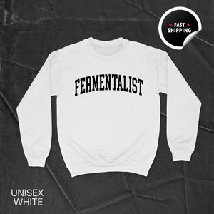 Può includere: Felpa unisex bianca con la scritta "FERMENTALIST" in nero, a forma di arco. La felpa ha maniche lunghe e girocollo. Le parole "UNISEX WHITE" sono stampate in basso. Un adesivo "FAST SHIPPING" si trova nell'angolo in alto a destra.