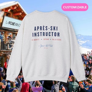 Op de afbeelding: Grijs sweatshirt met de tekst "Après-Ski Instructor" en "Après Ski Club Est. 2015" gedrukt op de achterkant. De tekst is in marineblauw.