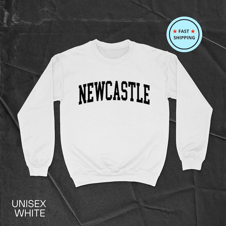 Puede incluir: Sudadera blanca unisex con la palabra "NEWCASTLE" en letras negras y en negrita en el pecho. La sudadera tiene mangas largas y cuello redondo. El texto "UNISEX WHITE" est&aacute; impreso en la parte inferior izquierda.