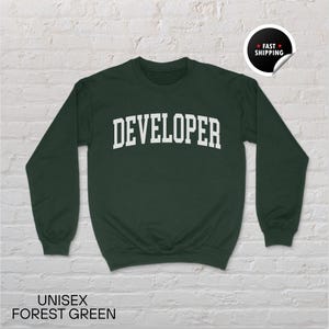May include: A forest green unisex sweatshirt with the word "DEVELOPER" printed in white block letters. The sweatshirt has long sleeves and a crew neck. The words "UNISEX FOREST GREEN" are printed at the bottom of the image.