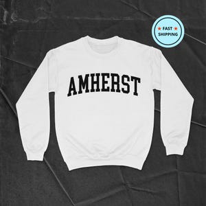 Könnte beinhalten: Weißer Pullover mit schwarzem Text, der "AMHERST" in einer College-Schriftart lautet.