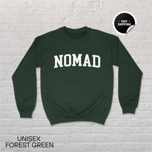 May include: Forest green unisex sweatshirt with the word "NOMAD" in white block letters. The sweatshirt has long sleeves and a crew neck. The words "UNISEX FOREST GREEN" are printed at the bottom of the image.