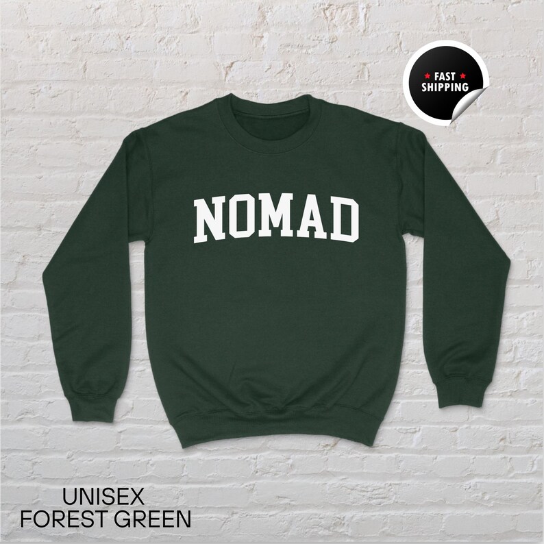 May include: Forest green unisex sweatshirt with the word "NOMAD" in white block letters. The sweatshirt has long sleeves and a crew neck. The words "UNISEX FOREST GREEN" are printed at the bottom of the image.