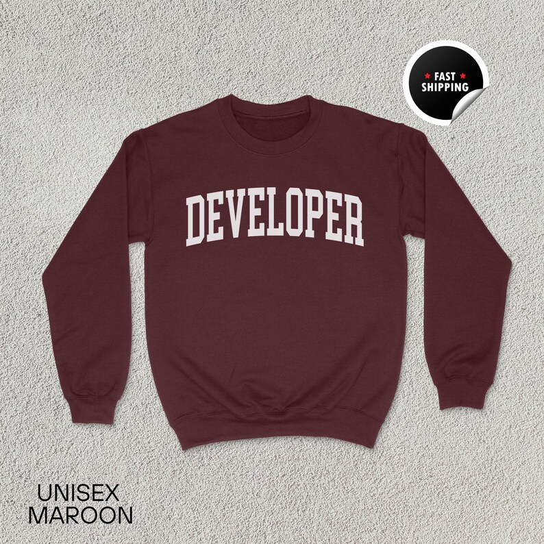 May include: Maroon unisex sweatshirt with the word "DEVELOPER" in white, bold, block letters across the chest. The sweatshirt has a crew neck and long sleeves. A "Fast Shipping" sticker is in the upper right corner.