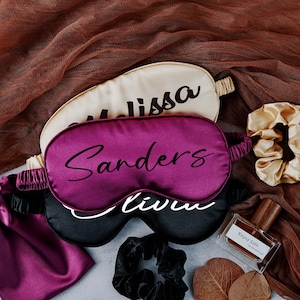 May include: Three satin sleep masks with personalised names, "Melissa", "Sanders", and "Olivia",  along with a small bottle of perfume labelled "Enjoy Life" and two hair scrunchies.